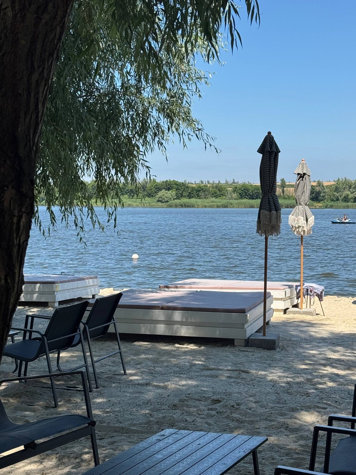 Лежаки в тіні верби та гідроцикл на воді